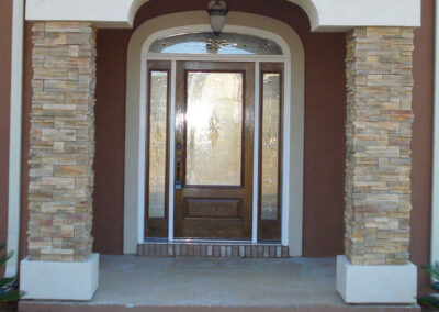 Grand entryway with a dark wood door, sidelights, and stone veneer surrounding the archway.