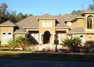 Large tan stucco house with stone accents, a multi-car garage, and a manicured lawn.