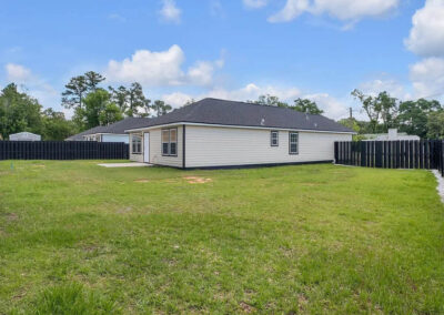 Backyard of a white house with a black fence, green grass, and white stone trim.