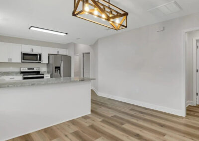 Modern kitchen with white cabinets, granite countertops, and stainless steel appliances from living room view.