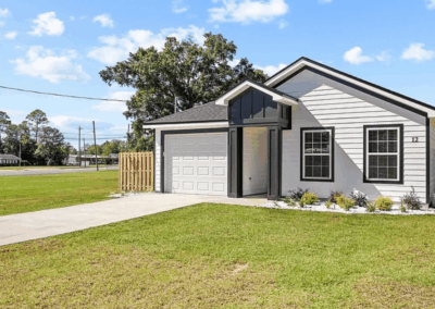 Small new single-family home with gray siding and a black roof in a grassy yard.