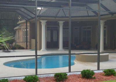 Screened-in backyard pool area with a black fence, mature landscaping, and a sunny patio.