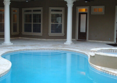 Curved blue swimming pool next to a patio with columns and a house entryway.