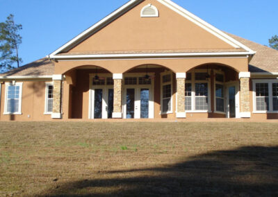 Tan stucco house with a covered entryway featuring multiple white columns and dark trim.