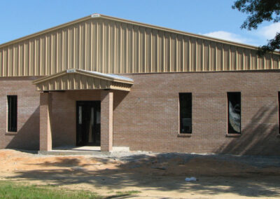Exterior view of a tan commercial building with a dark metal roof and a small covered entryway.