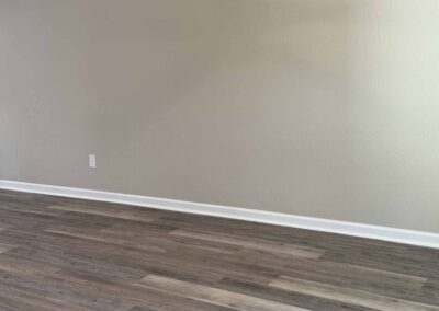 Empty room corner with light gray painted wall, white baseboard, two wall outlets, and wood-look vinyl plank flooring.
