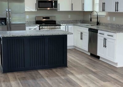 Kitchen with white cabinets, stainless-steel appliances, granite countertops, and a dark blue island on light wood-look vinyl flooring.
