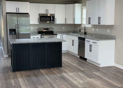 New kitchen with white shaker cabinets, black island, stainless appliances, granite countertops, and wood-look vinyl flooring.
